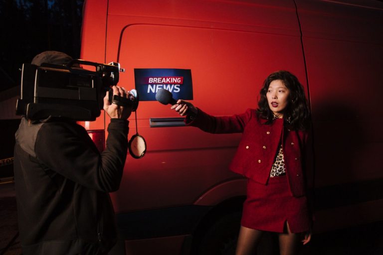 Asian female reporter with cameraman conducting a nighttime news broadcast beside a news van.