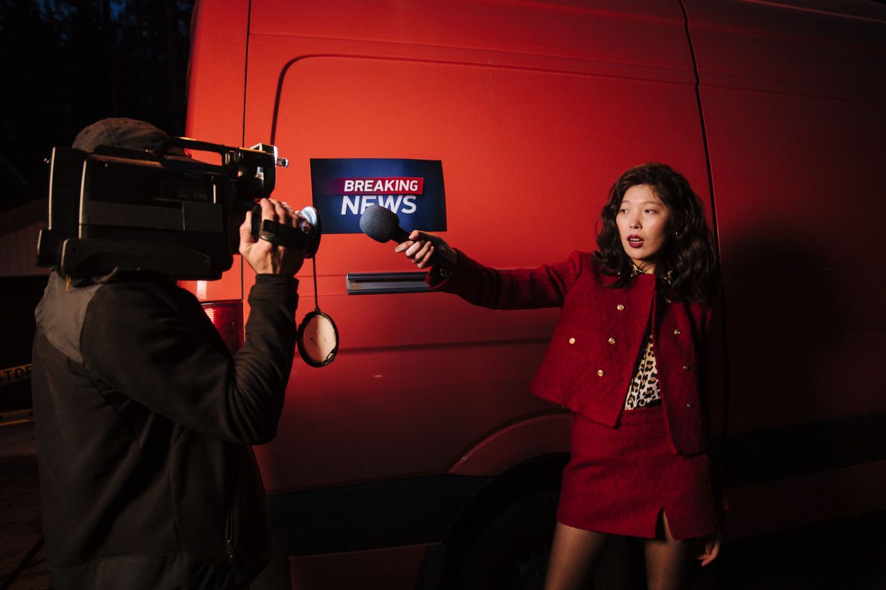 Asian female reporter with cameraman conducting a nighttime news broadcast beside a news van.